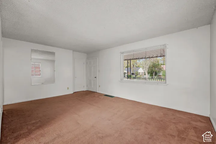 Carpeted flooring, white painted walls, and a large window with horizontal blinds