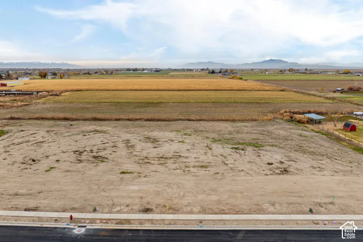 Flat building lot with street frontage, sidewalk, and mountain backdrop