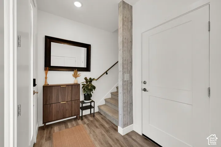 White interior doors, wood-finish flooring, white walls, recessed lighting, and a contemporary stair handrail