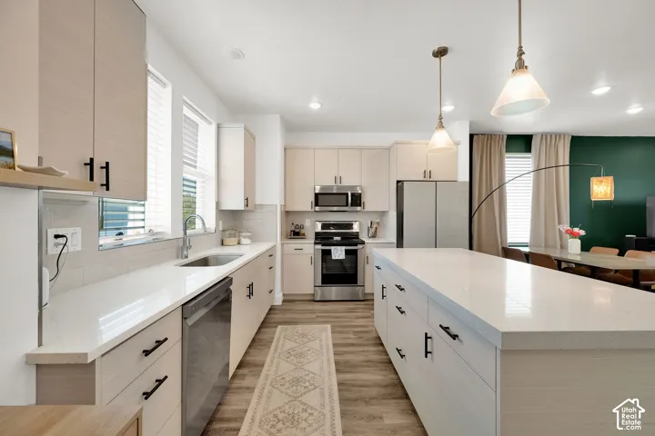 Contemporary kitchen featuring light wood-finish cabinetry, stainless steel appliances, a large center island with a light-toned countertop, and recessed lighting