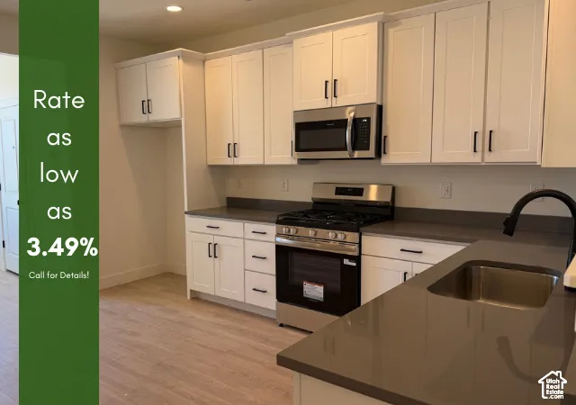 White shaker cabinetry, stainless steel appliances, dark stone countertops, undermount sink, and wood-finish flooring