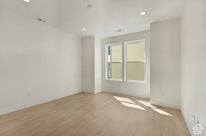 Bright, light-filled room showcasing warm wood-finish flooring, clean white walls, and recessed ceiling lighting