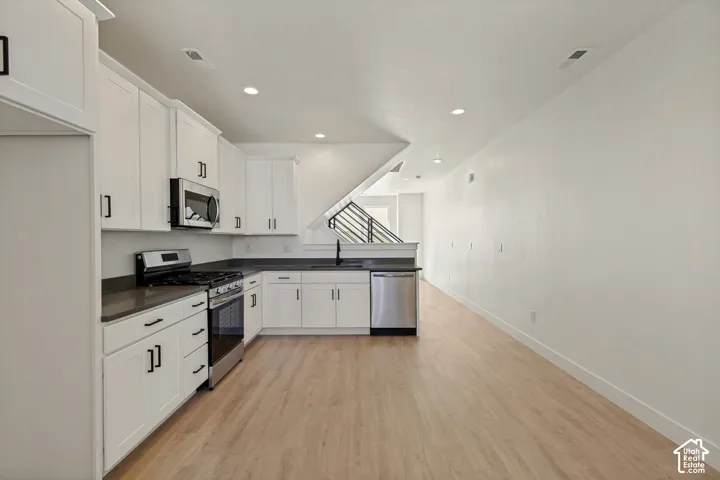 Kitchen featuring white cabinetry, dark countertops, stainless steel appliances, and wood-finish flooring
