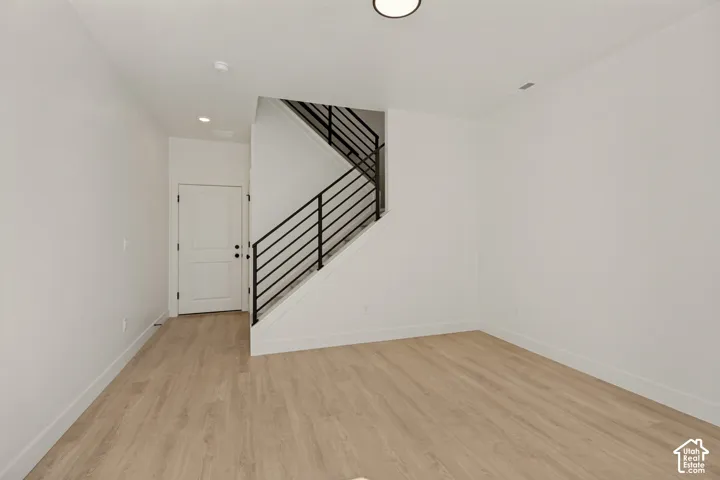 Light wood-finish flooring, white walls, modern black metal stair railing, and a contemporary flush-mount ceiling light