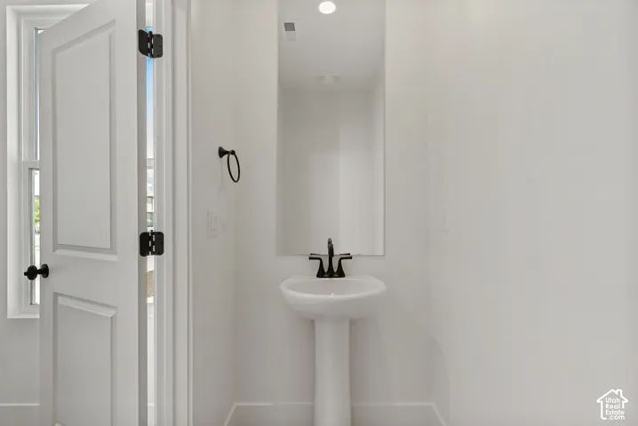 Pedestal sink with a matte black faucet, wall-mounted mirror, and white paneled door