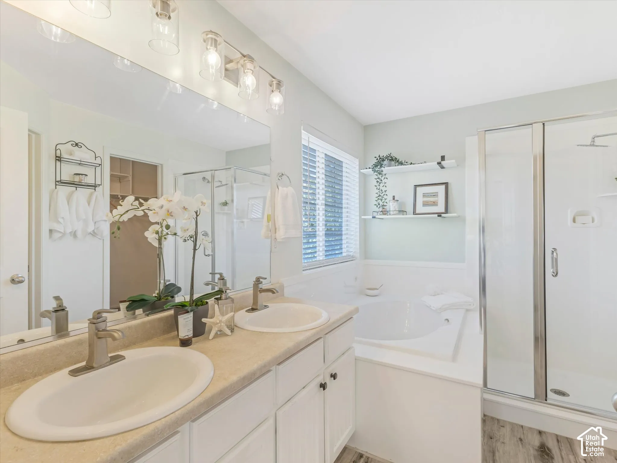 Dual vanity with undermount sinks, a built-in soaking tub, a separate glass-enclosed shower, wood-finish flooring, and a large mirror