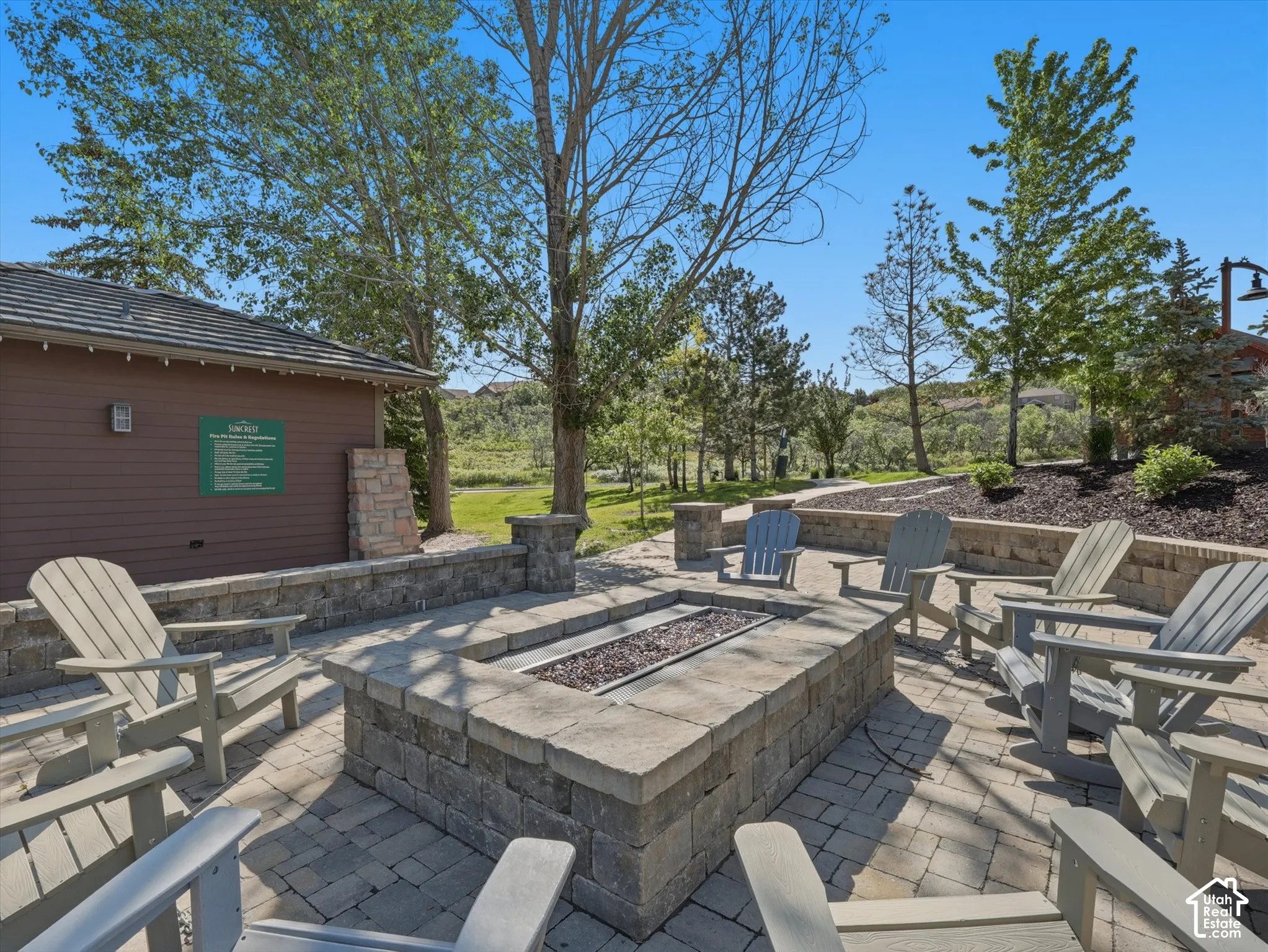 Paver patio with a built-in stone fire pit, surrounded by mature trees and landscaping