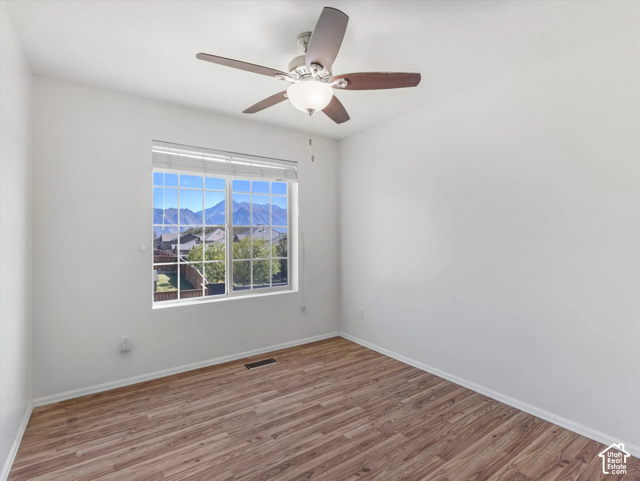 Room featuring a ceiling fan with integrated lighting, wood-finish flooring, and a window offering a mountain backdrop