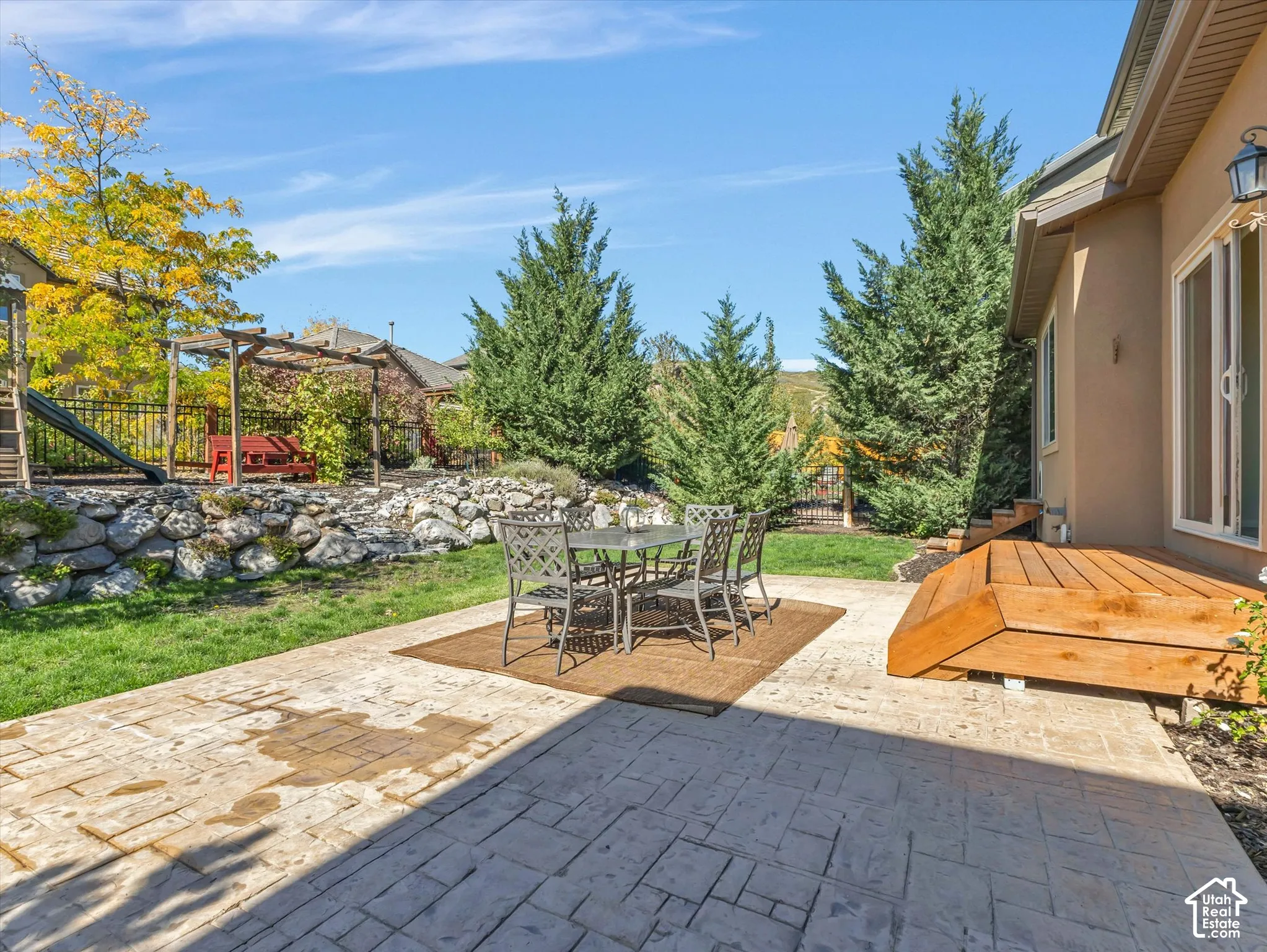 Stamped concrete patio with a wood deck, manicured lawn, and mature evergreen trees