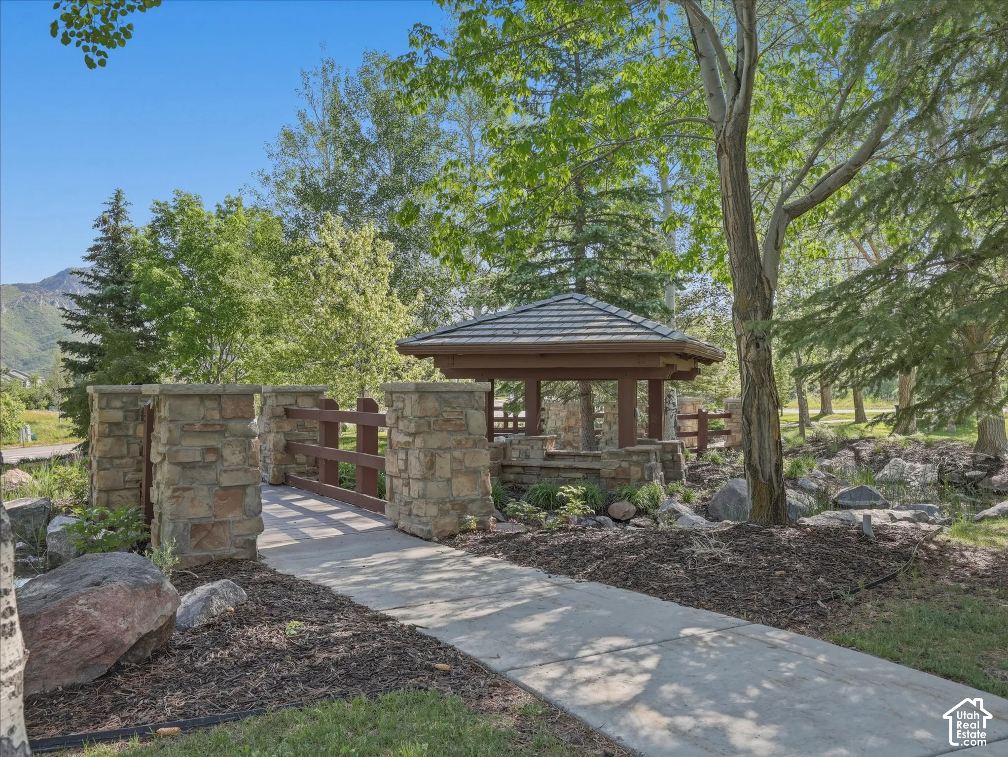 Stone pillar bridge with wood railing and adjacent gazebo, surrounded by mature trees and landscaping
