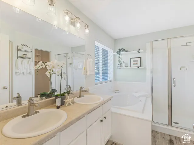 Dual vanity with undermount sinks, a built-in soaking tub, a separate glass-enclosed shower, wood-finish flooring, and a large mirror