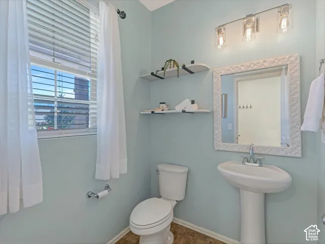 Pedestal sink with chrome fixtures, framed mirror, wall-mounted light fixture, built-in shelving, and window with blinds