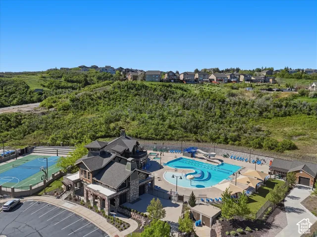 Community recreation center featuring a multi-sport court, expansive swimming pool with water slides, structured parking, and surrounding natural landscaping