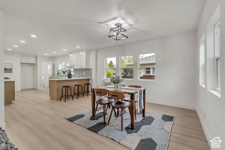Light wood-finish flooring throughout, white walls, recessed ceiling lighting, kitchen island with seating, and a decorative ceiling fixture