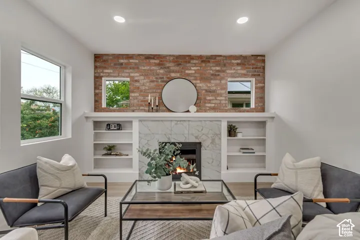 Recessed lighting, exposed brick accent wall, built-in shelving, fireplace with decorative tile surround, and wood-finish flooring