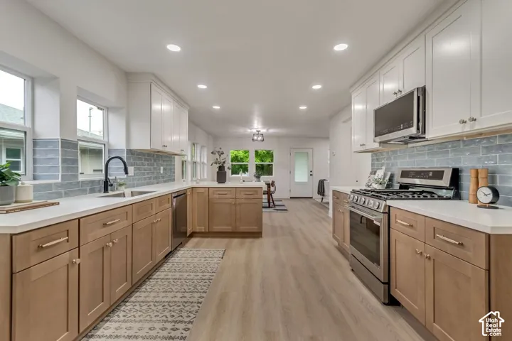 Contemporary kitchen with two-tone cabinetry, stainless steel appliances, light-toned countertops, tile backsplash, and recessed lighting