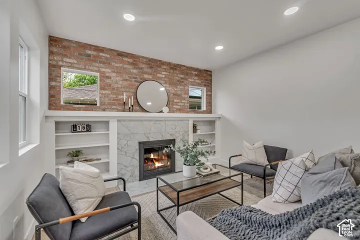 Exposed brick accent wall, built-in shelving, fireplace with stone surround, recessed ceiling lighting, and multiple windows