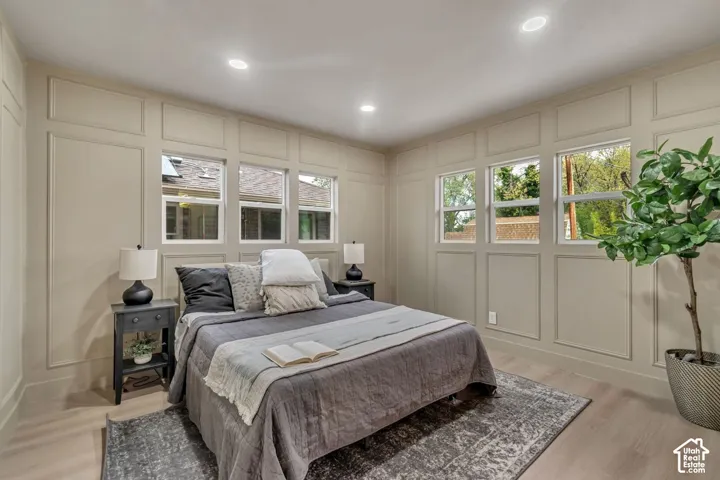 Recessed ceiling lighting, decorative wall paneling, light wood-finish flooring, multiple windows, and a ceiling fan