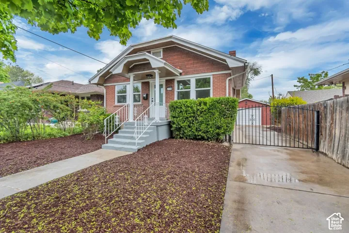 Brick exterior with white trim, front porch with white railings, paved driveway, wrought iron gate, and detached garage