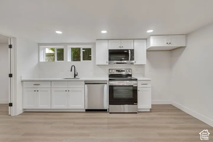 Modern kitchen featuring white shaker-style cabinetry, stainless steel appliances including a dual oven configuration, quartz countertops, an undermount sink with contemporary faucet, recessed ceiling lighting, and wood-finish flooring throughout