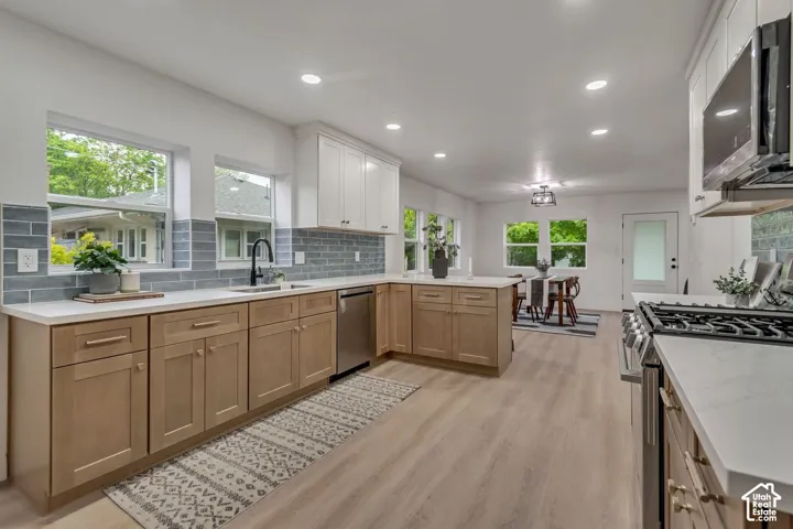 Contemporary kitchen featuring light wood-finish flooring, two-tone cabinetry, stainless steel appliances, and a subway tile backsplash