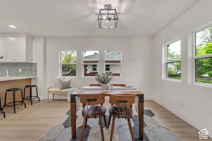 Bright, open dining area showcasing a wood-finish dining table with upholstered chairs, light wood-finish flooring throughout, and abundant natural light from multiple large windows