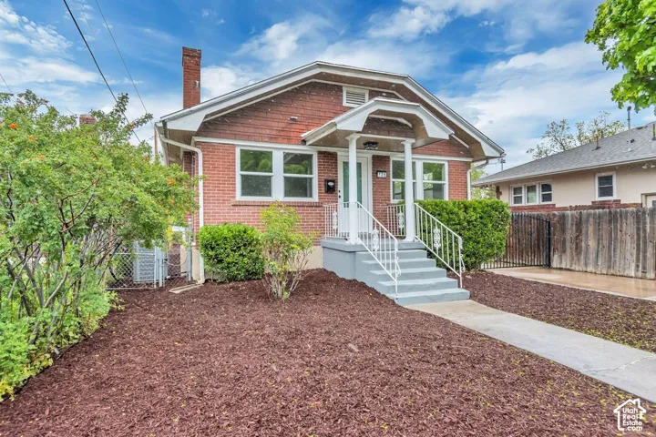 Charming brick home featuring a welcoming front entrance with white-trimmed arched doorway and multi-pane windows, complemented by a manicured front landscape with mature plantings and mulched beds
