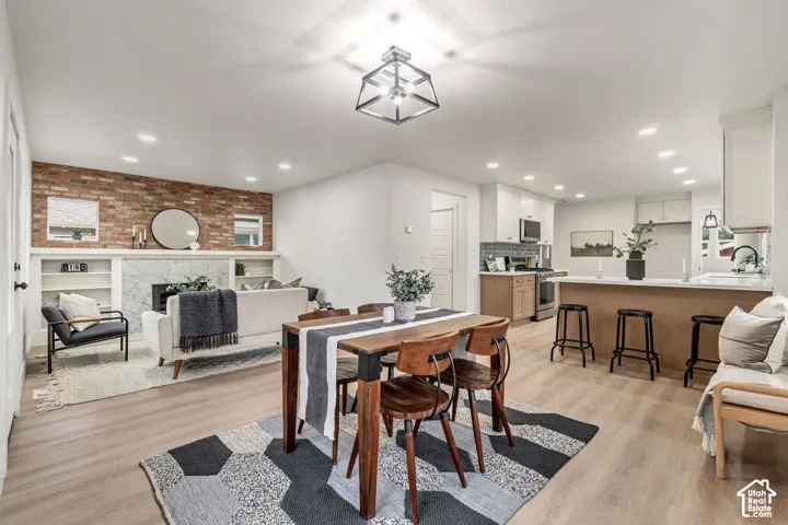 Open-concept living space featuring wood-finish flooring, a brick accent wall, built-in shelving, a kitchen island with seating, and recessed lighting
