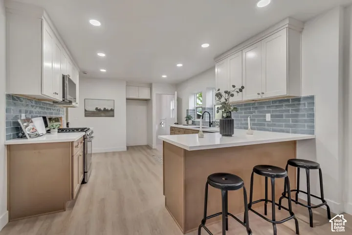 Kitchen featuring white upper cabinetry, light wood-finish lower cabinetry, white countertops, and a blue subway tile backsplash