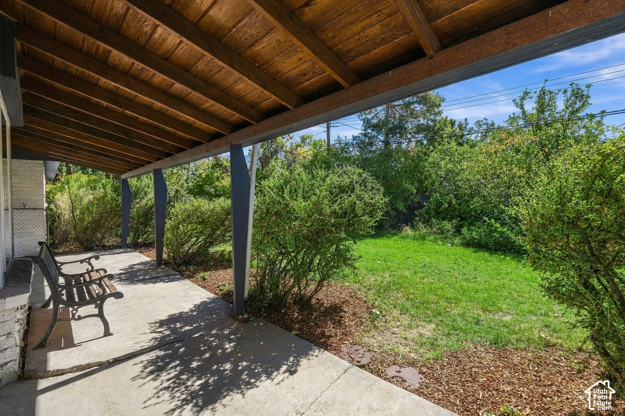 Covered back patio with a concrete surface, supported by architectural posts, featuring an exposed wood-finish ceiling