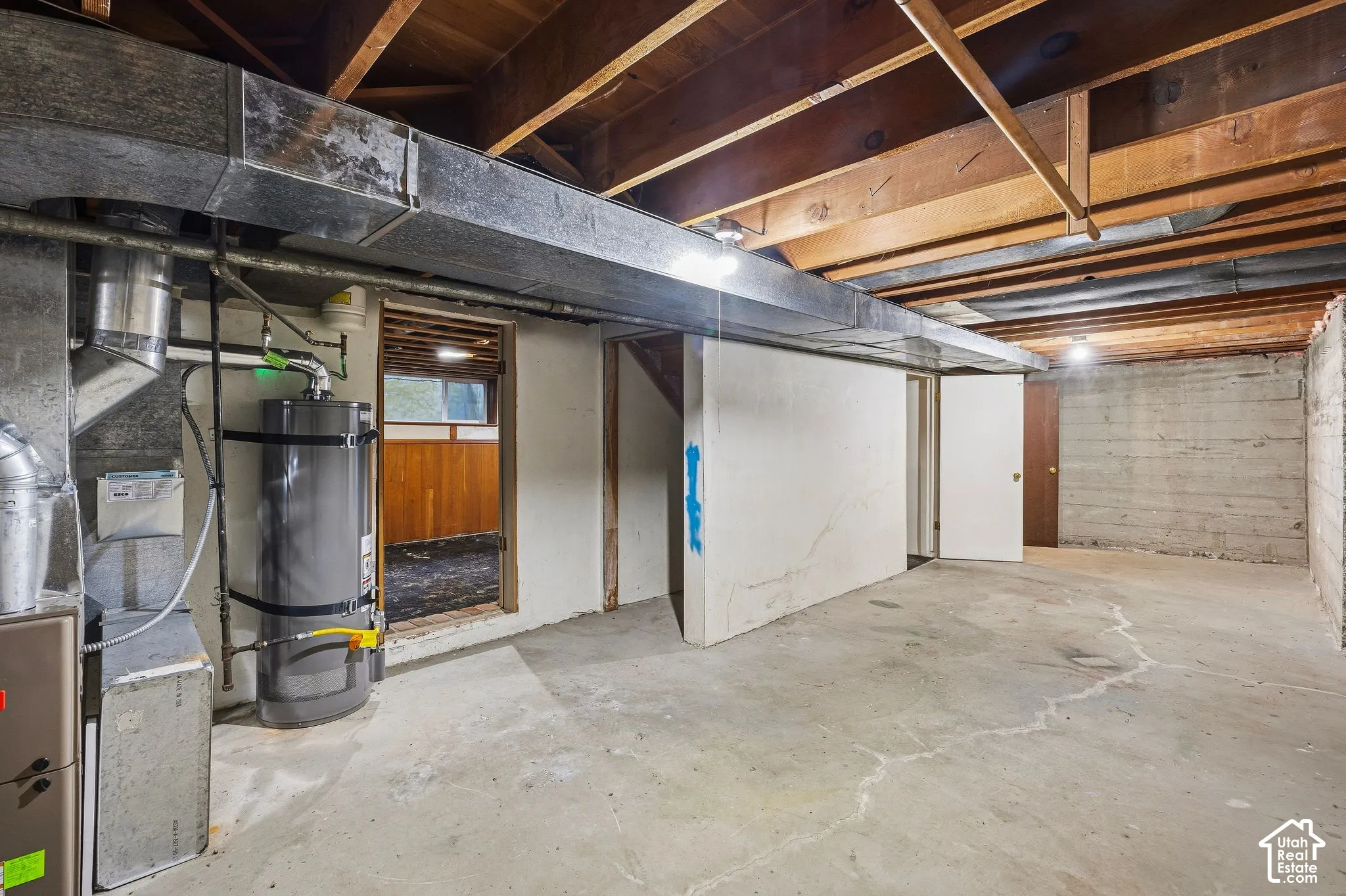 Unfinished half of the basement featuring exposed ceiling joists, concrete flooring, and a mechanical room