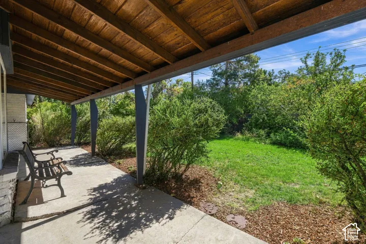Covered back patio with a concrete surface, supported by architectural posts, featuring an exposed wood-finish ceiling