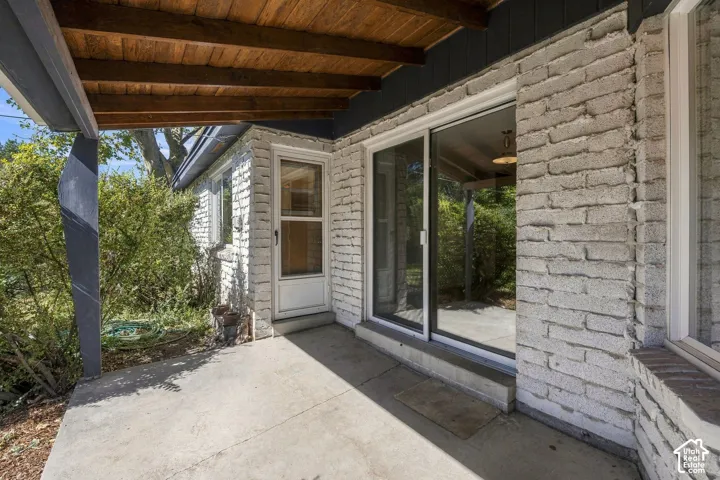 Covered back patio with exposed wood ceiling beams, concrete flooring, and brick exterior walls