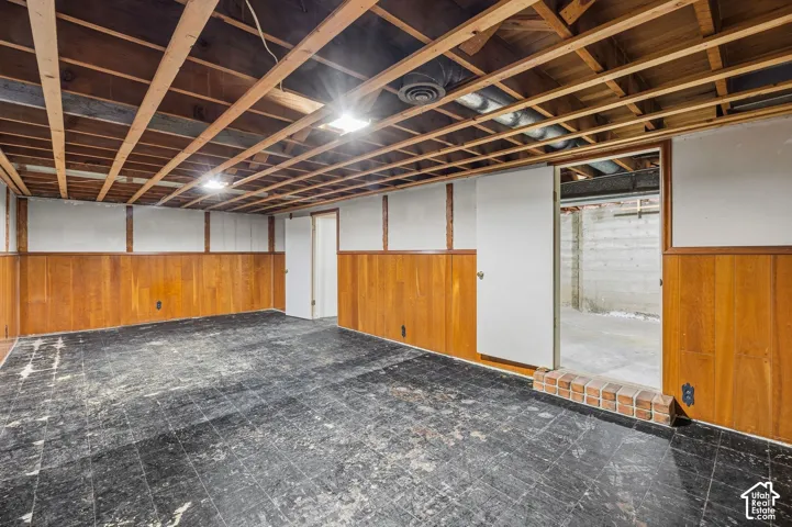 Part-finished half of the basement featuring exposed wood joist ceiling, wood paneling, and interior doors