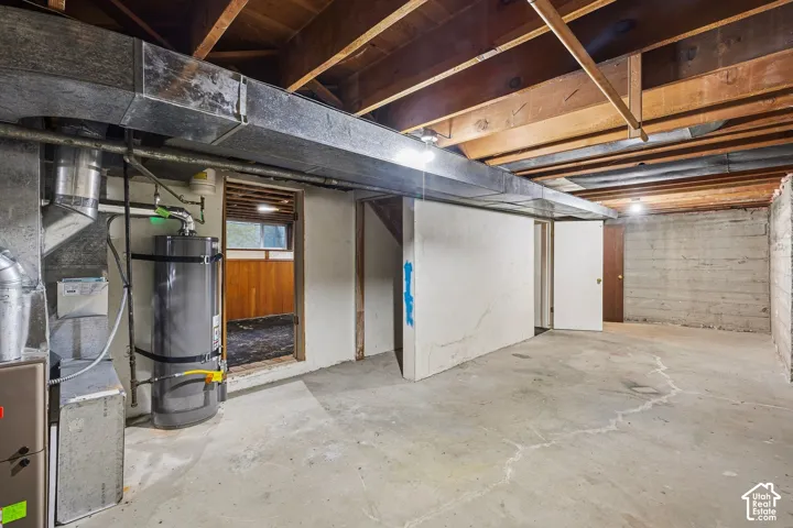 Unfinished half of the basement featuring exposed ceiling joists, concrete flooring, and a mechanical room
