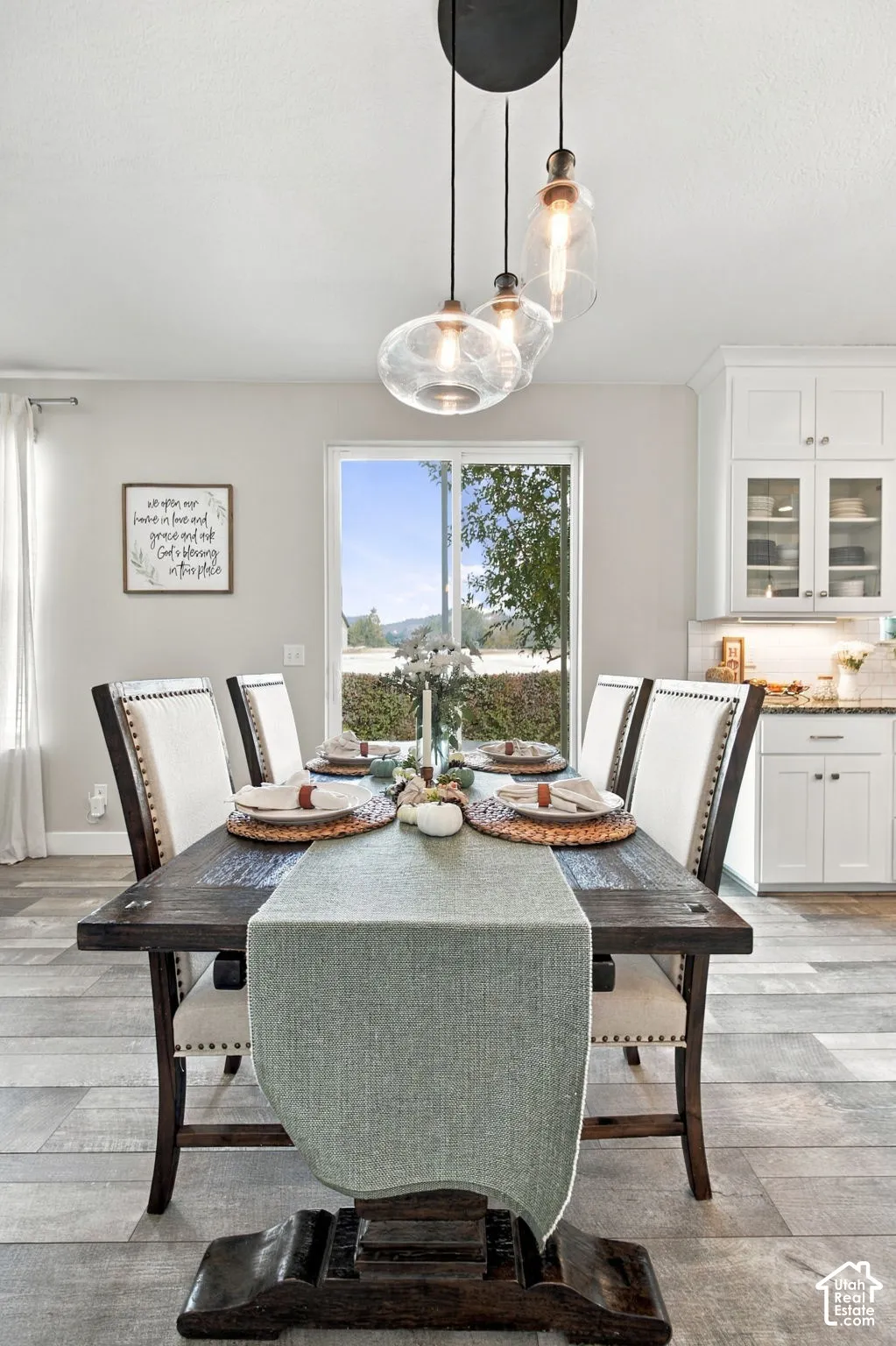 Wood-finish flooring, white cabinetry with glass-front uppers, and clear glass pendant lighting