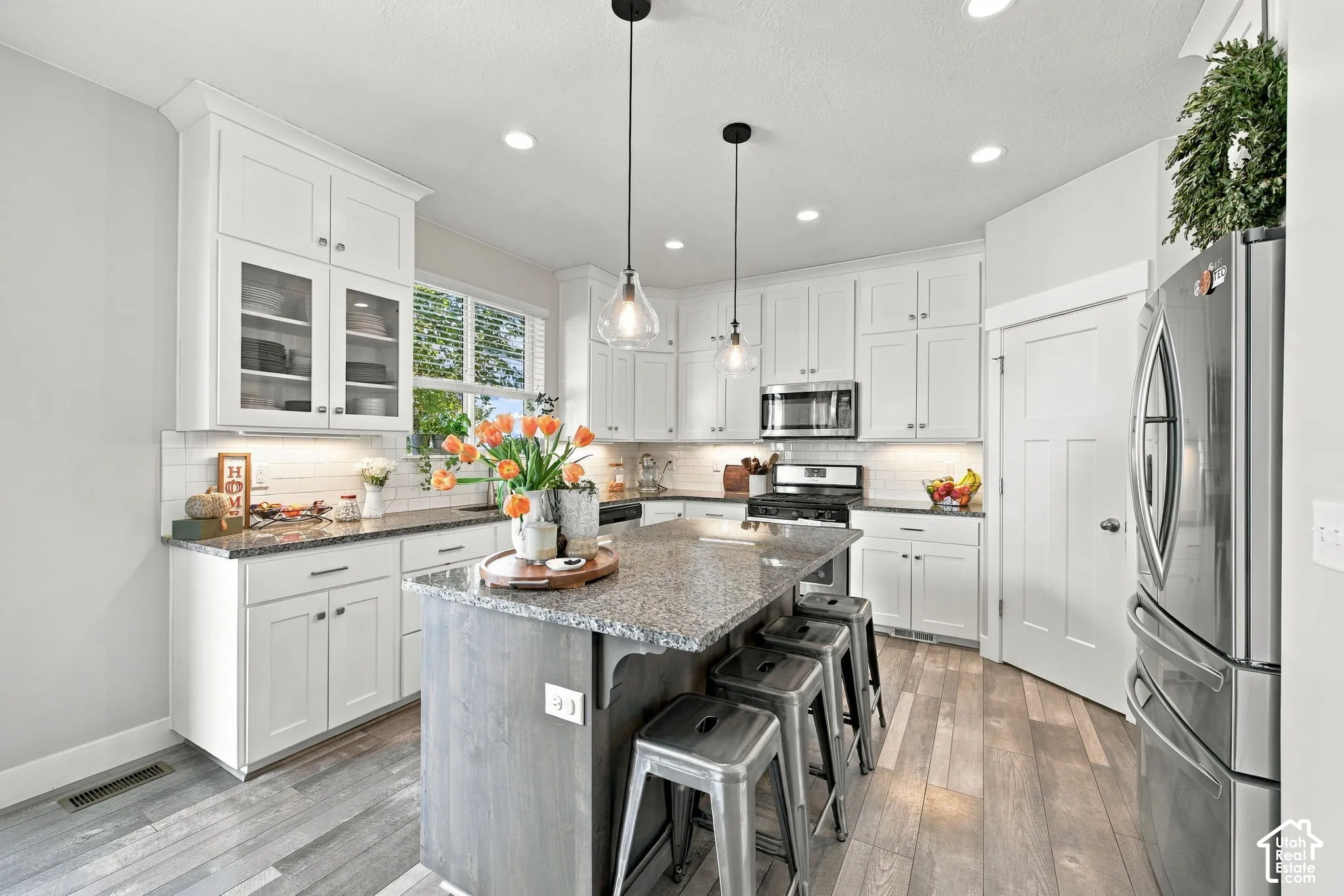 White cabinetry, stainless steel appliances, central island with seating, recessed lighting, and wood-finish flooring