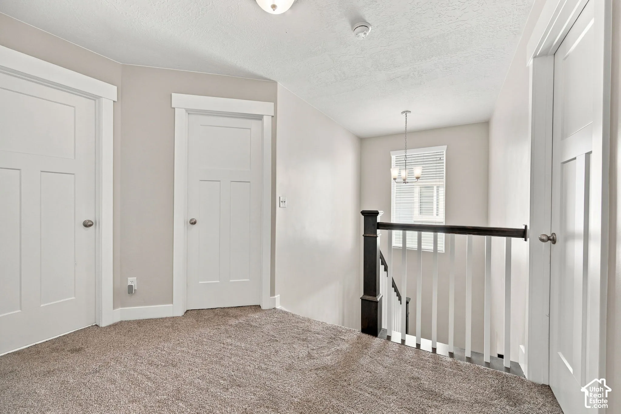 Carpeted landing featuring white paneled doors with contrasting trim, a two-tone stair railing, and a window with blinds