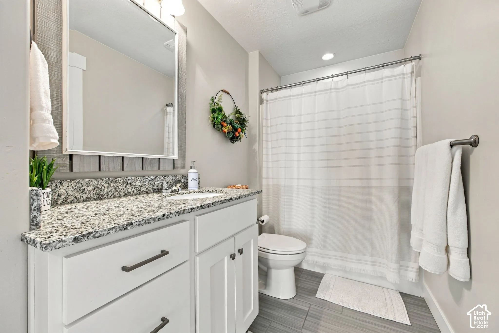 White shaker-style vanity with dark hardware, granite-look countertop, and undermount sink