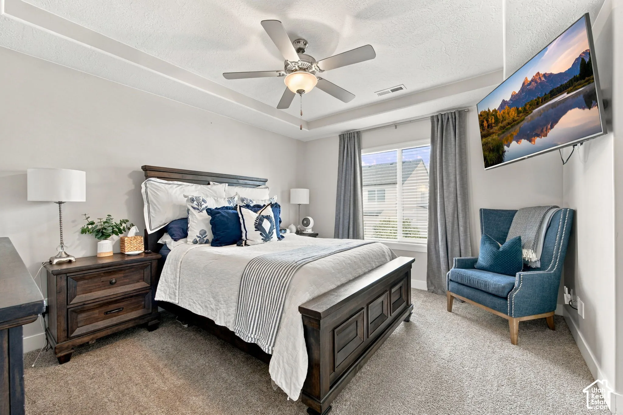 Tray ceiling with a ceiling fan, wall-mounted television, and window with blinds