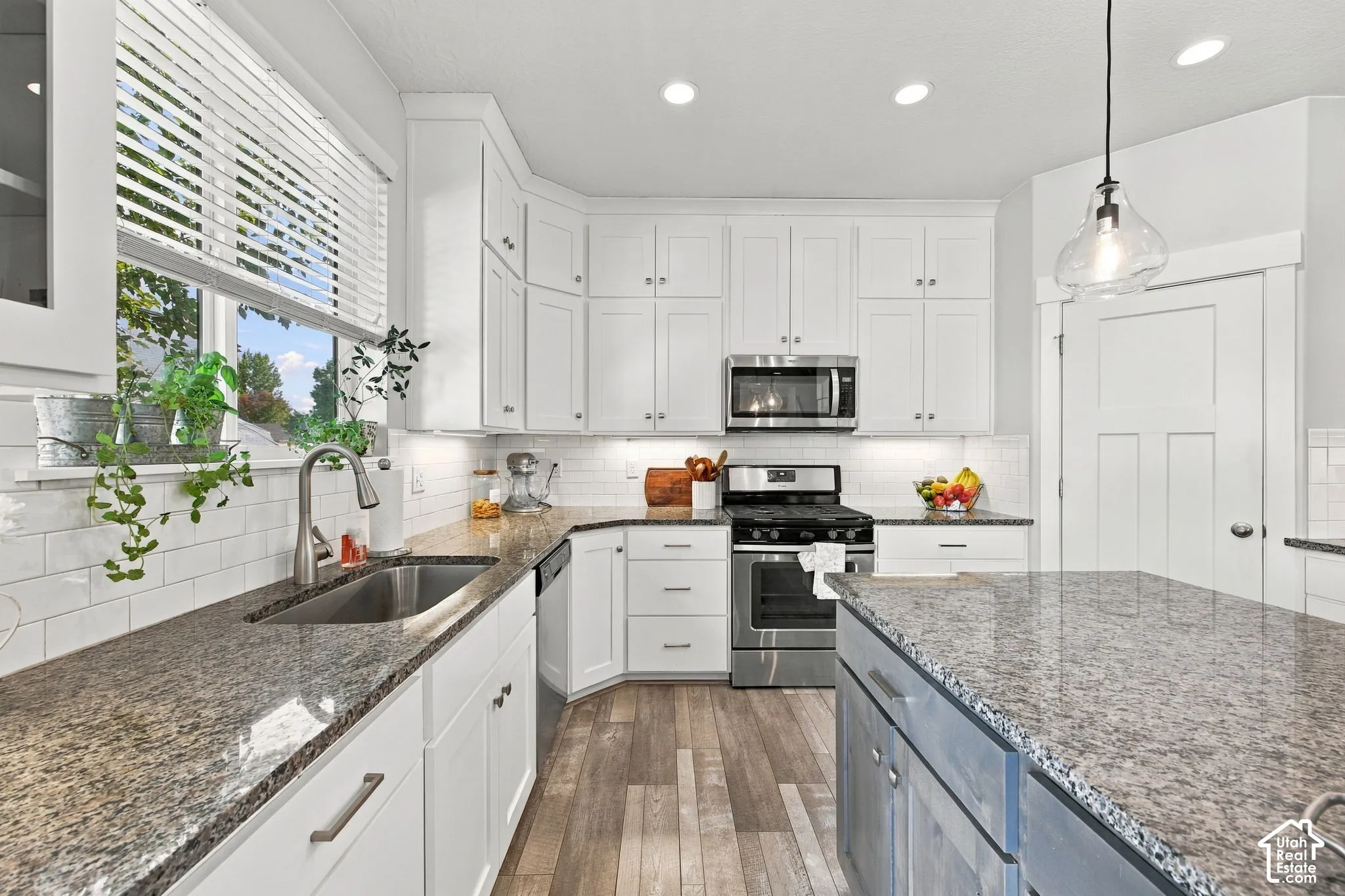 White cabinetry, stainless steel appliances, wood-finish flooring, undermount sink, and durable countertops