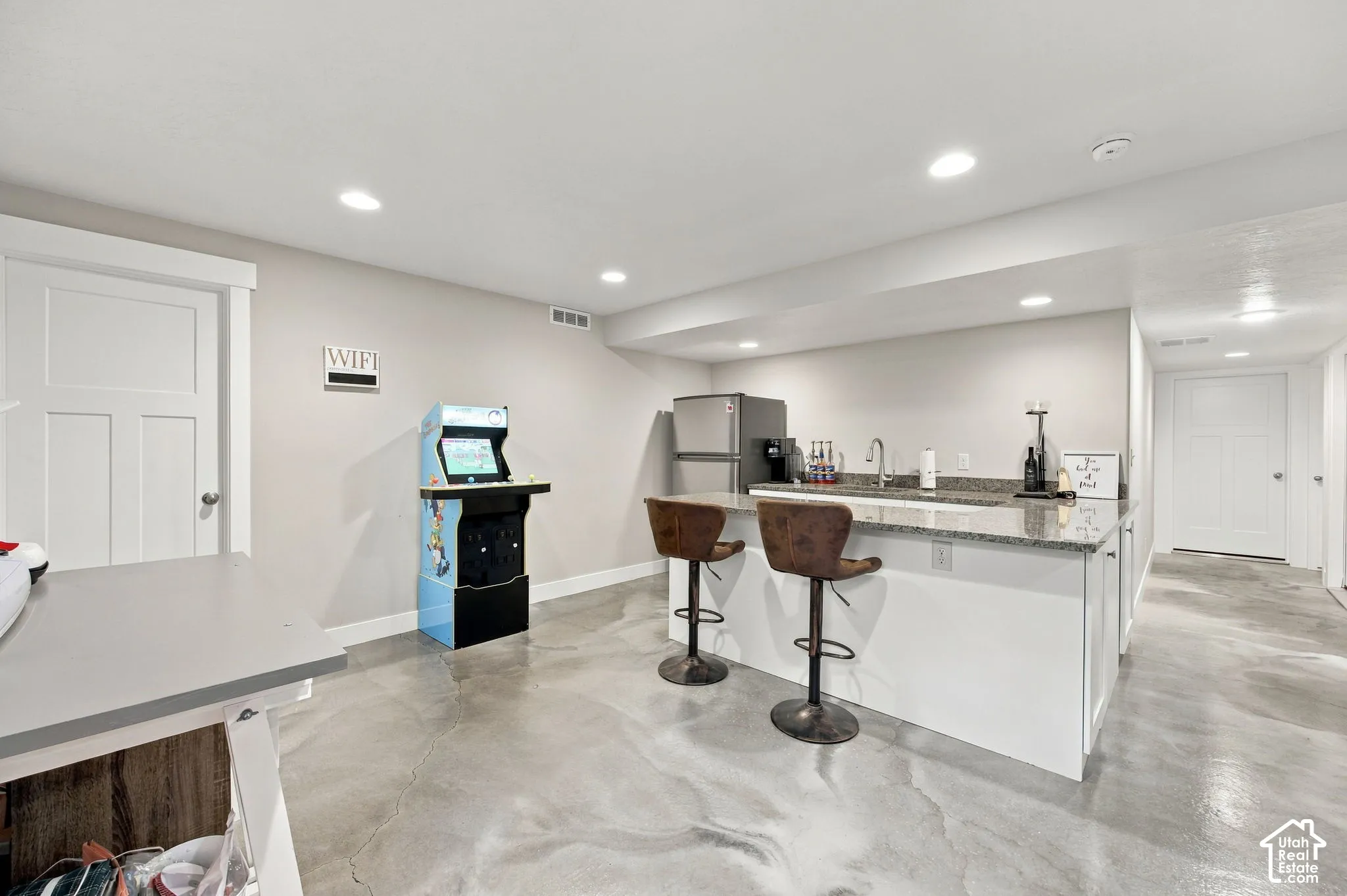 Recessed lighting, light gray walls, white base cabinetry, polished concrete flooring, and solid surface countertops