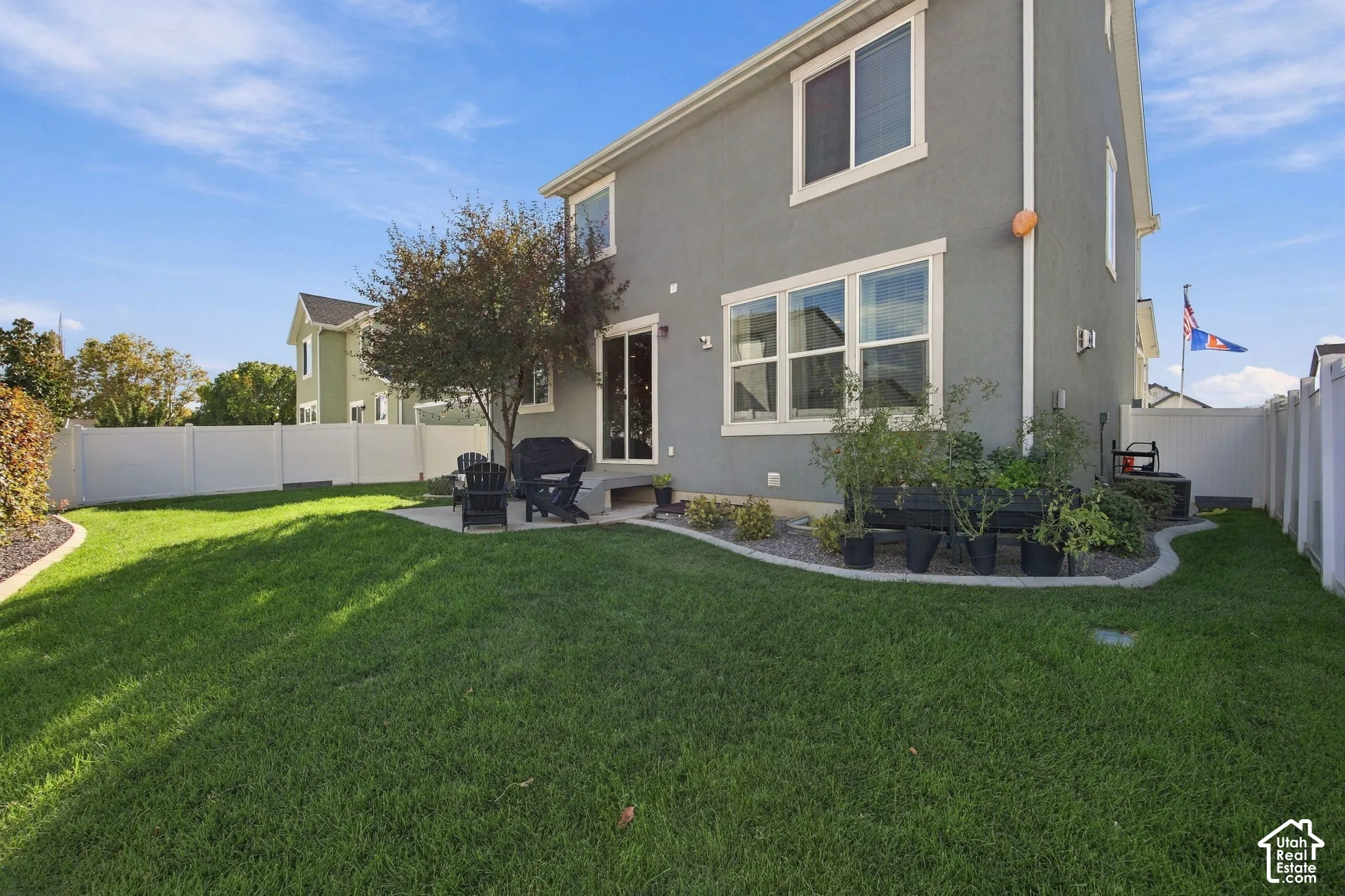 Expansive grassy yard with a white vinyl fence, concrete patio, and mature tree landscaping
