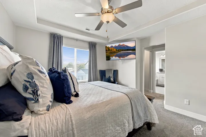 Recessed ceiling with an integrated ceiling fan, carpet flooring, and a window with blinds and drapes