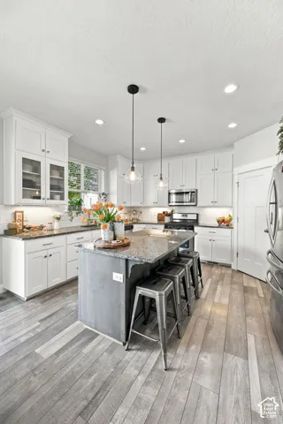 White cabinetry with glass-front accents, dark wood-finish island with seating, recessed lighting, and wood-finish flooring