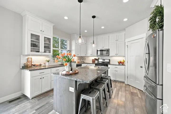 White cabinetry, stainless steel appliances, central island with seating, recessed lighting, and wood-finish flooring