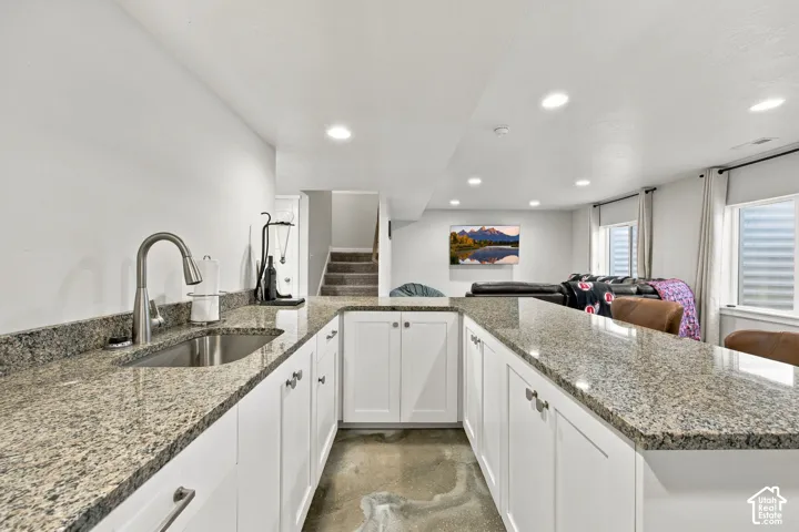 Wet bar featuring a stainless steel sink, gooseneck faucet, light granite-style countertops, and white shaker-style cabinetry with silver hardware