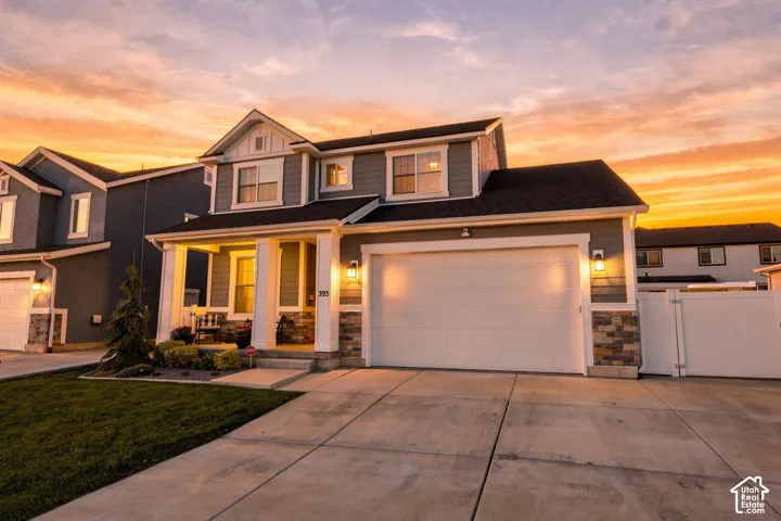 Two-story residence featuring a gray exterior with stone accents, a two-car garage, and a covered front porch