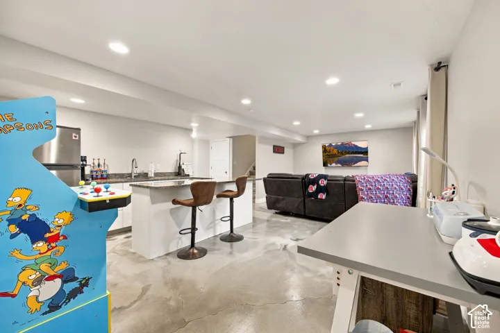 Recessed lighting, light gray walls, built-in lower cabinetry, a stainless steel refrigerator, and stone-finish countertops