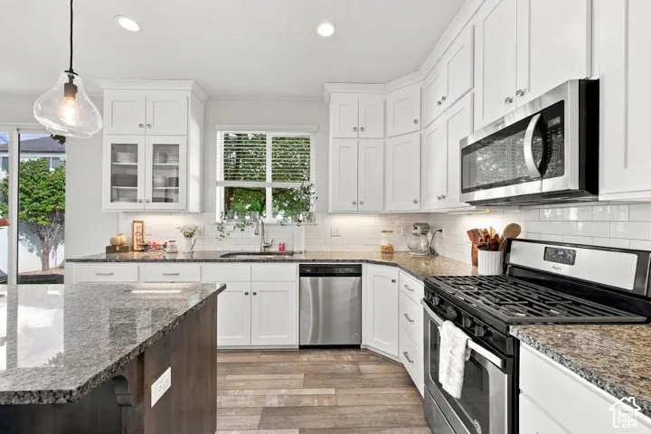 Kitchen featuring white cabinetry, granite countertops, stainless steel appliances, wood-finish flooring, and subway tile backsplash